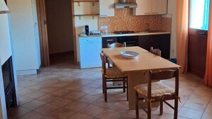 A kitchen with wooden beams, a tiled floor, a dining table with chairs, and a window with curtains.