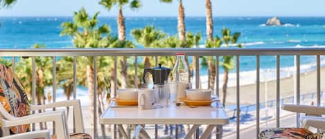 Ein Balkon mit Tisch für Zwei, mit Blick auf einen Strand mit Palmen und das Meer.