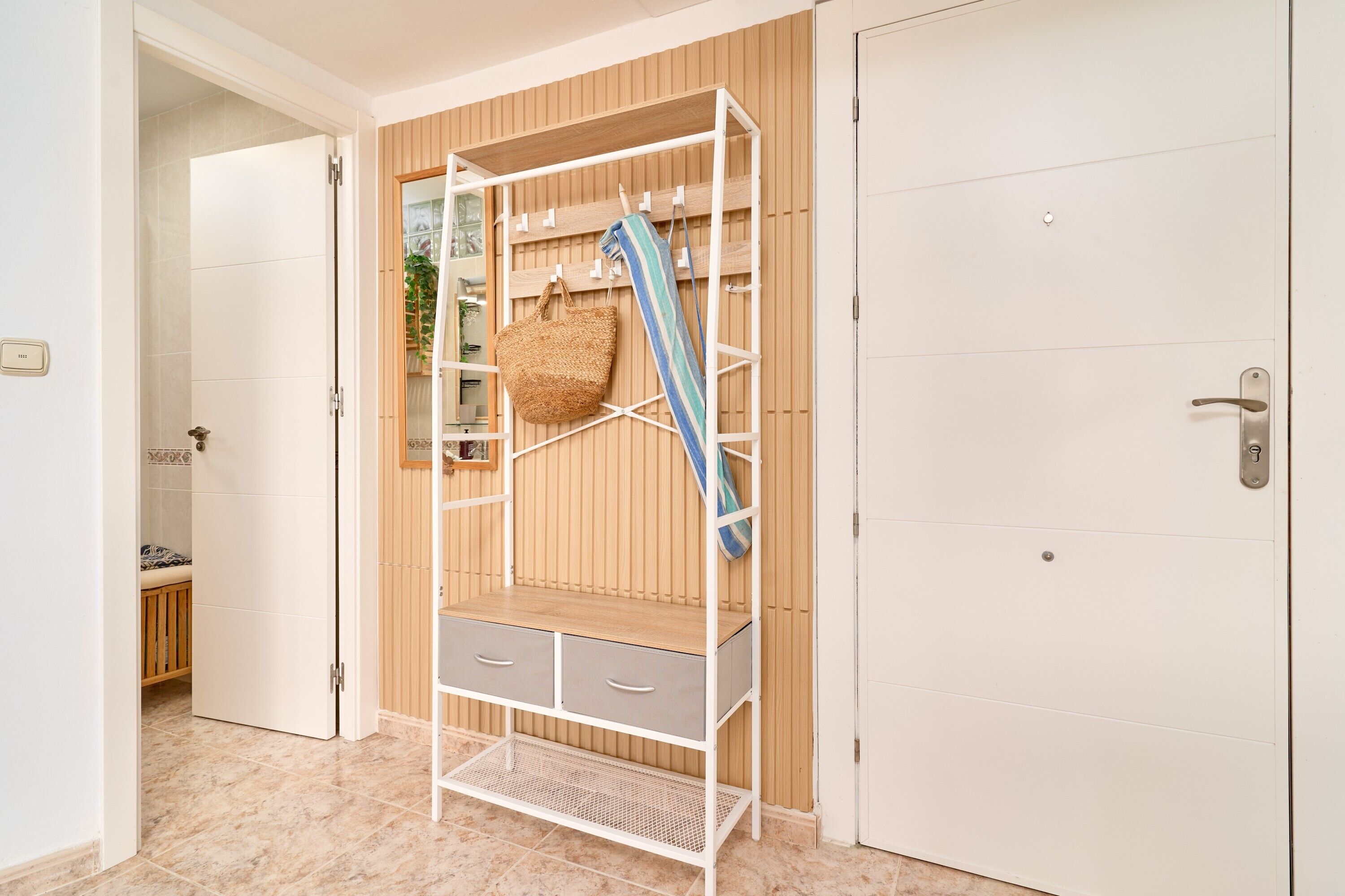A room with a white wardrobe, a wooden panel wall, a white door, and a small bench in the background.
