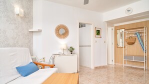 A modern hotel room with a white sofa, a wooden table, a wall-mounted lamp, a small desk with a lamp, a mirror, and a wooden door with a towel rack. - Apartment 'Góndolas Costa Tropical' with Sea View, Wi-Fi and Air Conditioning (ALMUÑECAR)