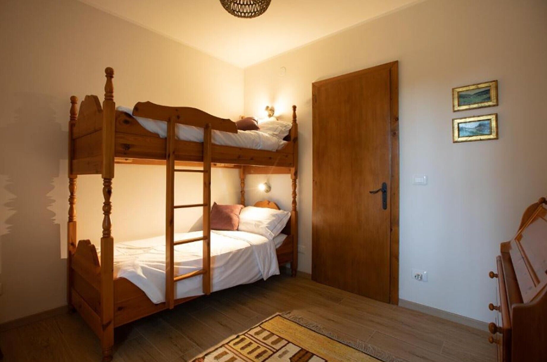 Ein Schlafraum mit Etagenbetten, einer Holztür, einem kleinen Teppich und zwei gerahmten Bildern an der Wand.