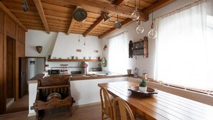 A rustic kitchen with wooden beams, a wooden dining table, and a hanging light fixture. - Double Suite "Collio Bianco" with Private Garden (Mossa)
