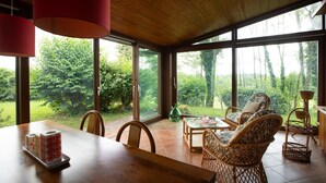 A dining area with a wooden table, wicker chairs, and a view of greenery through large windows. - Double Suite "Collio Bianco" with Private Garden (Mossa)