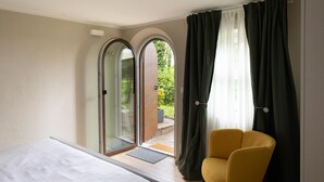 A bedroom with a bed, a yellow chair, and a sliding glass door leading to an outdoor area. - Double Suite "Collio Bianco" with Private Garden (Mossa)