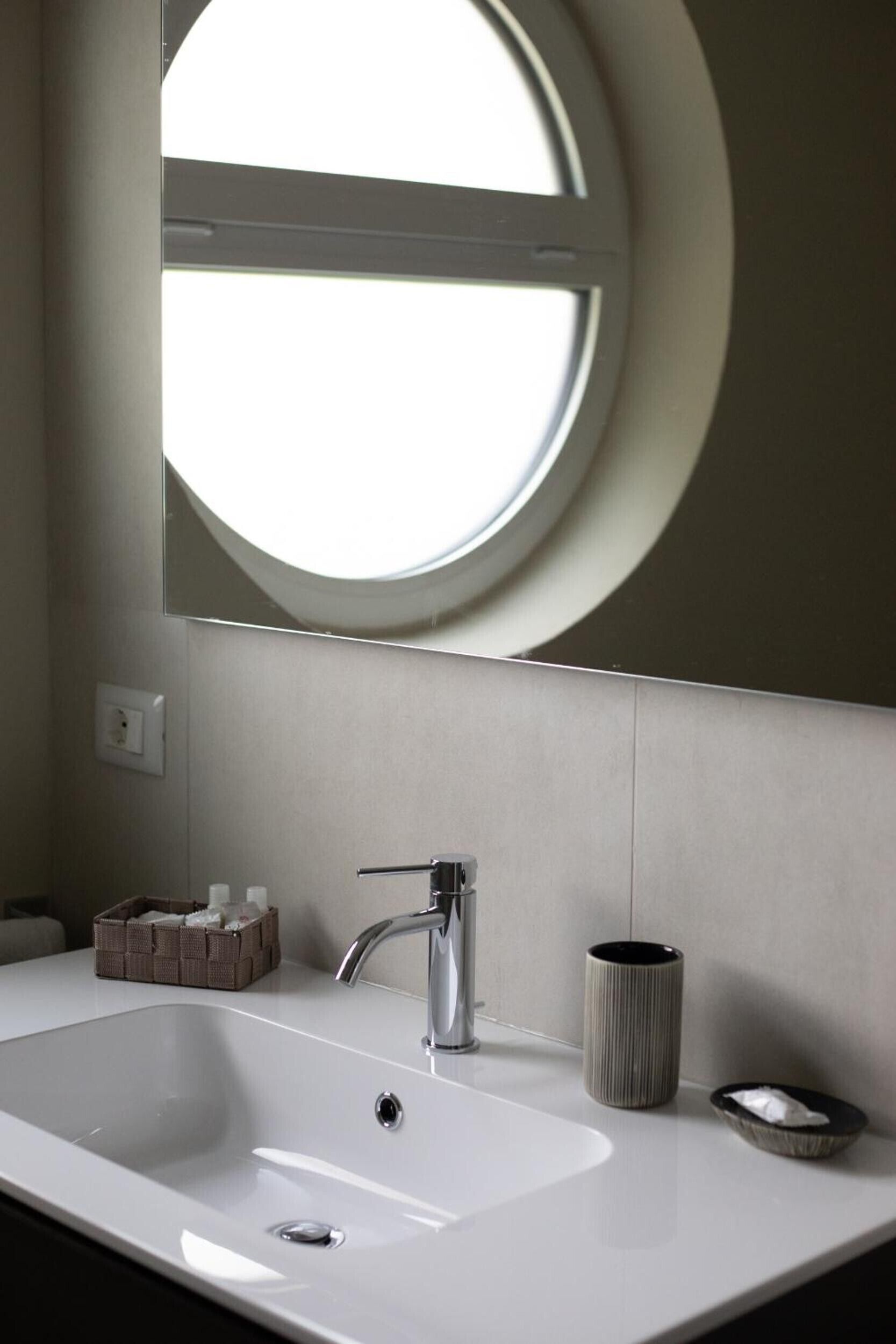 Un bany amb un lavabo blanc, un mirall rodó i una finestra.