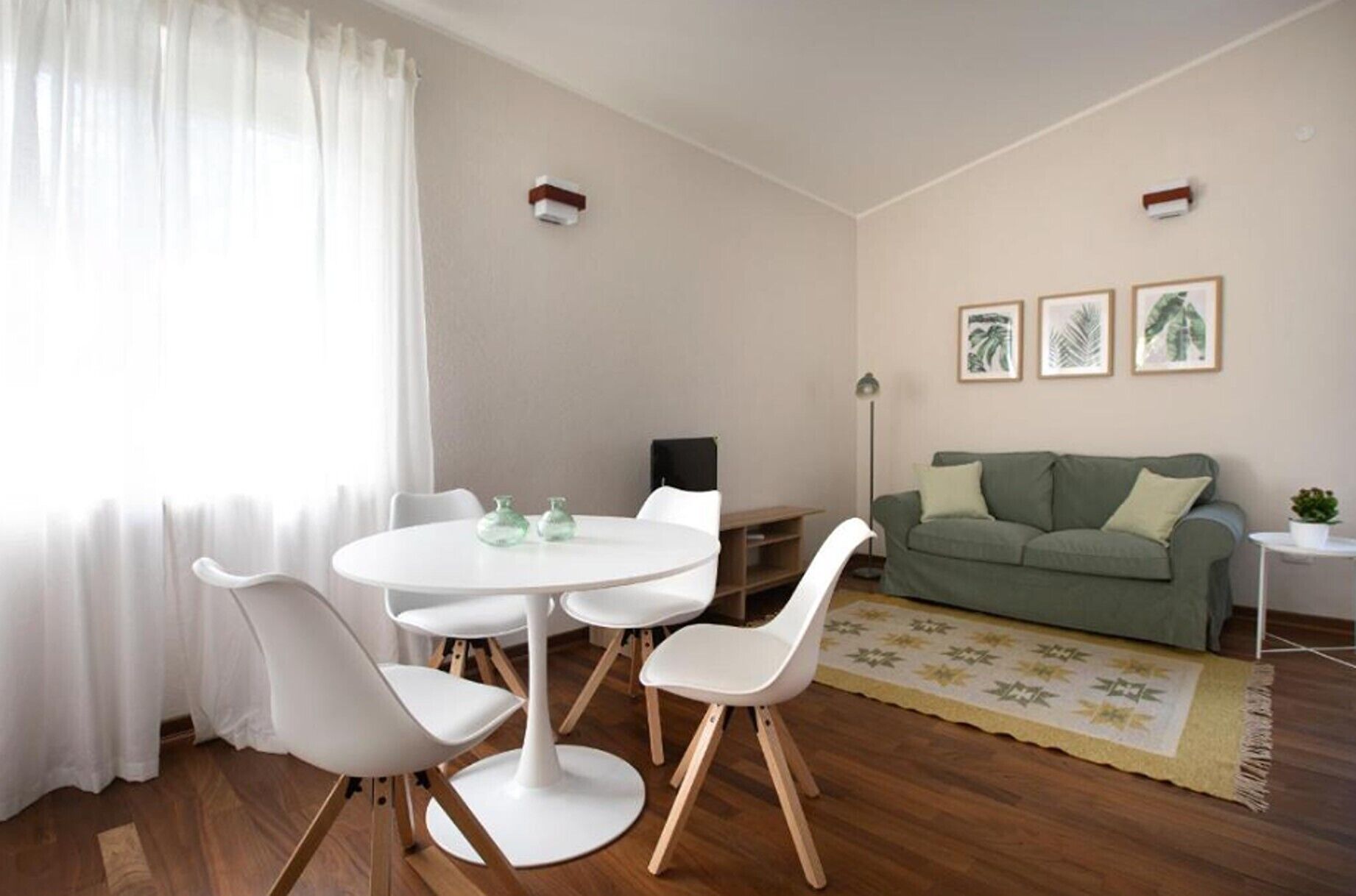 A living room with a round table, white chairs, a green sofa, and a small side table.