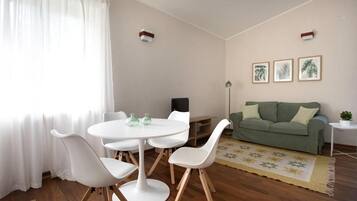 A living room with a round table, white chairs, a green sofa, and a small side table.