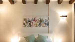 A bed with two pillows, a nightstand, a wall-mounted light, and a floral artwork above the bed.