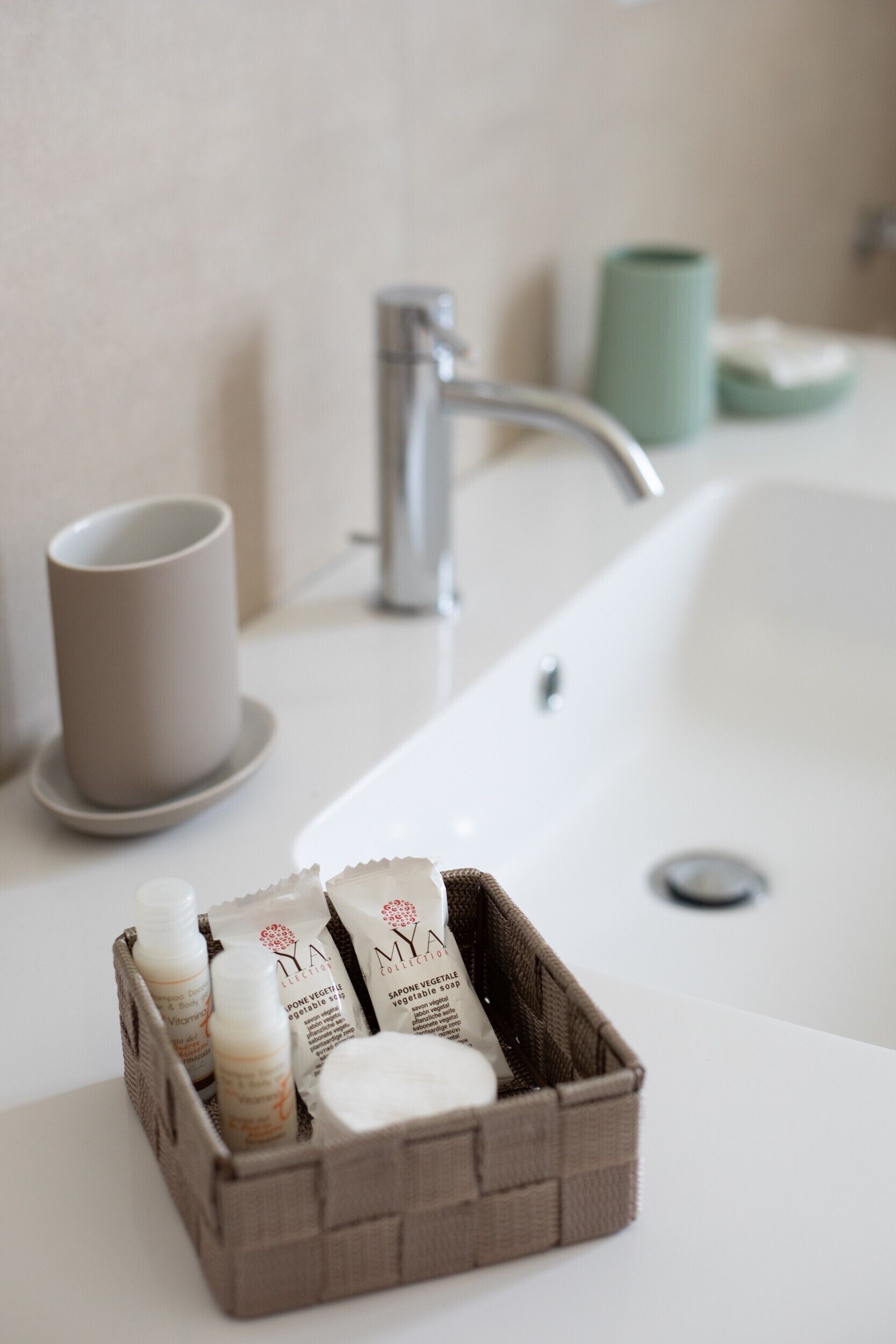 Un lavabo de salle de bain avec un receveur blanc, une tasse beige et un panier marron contenant des articles de toilette.