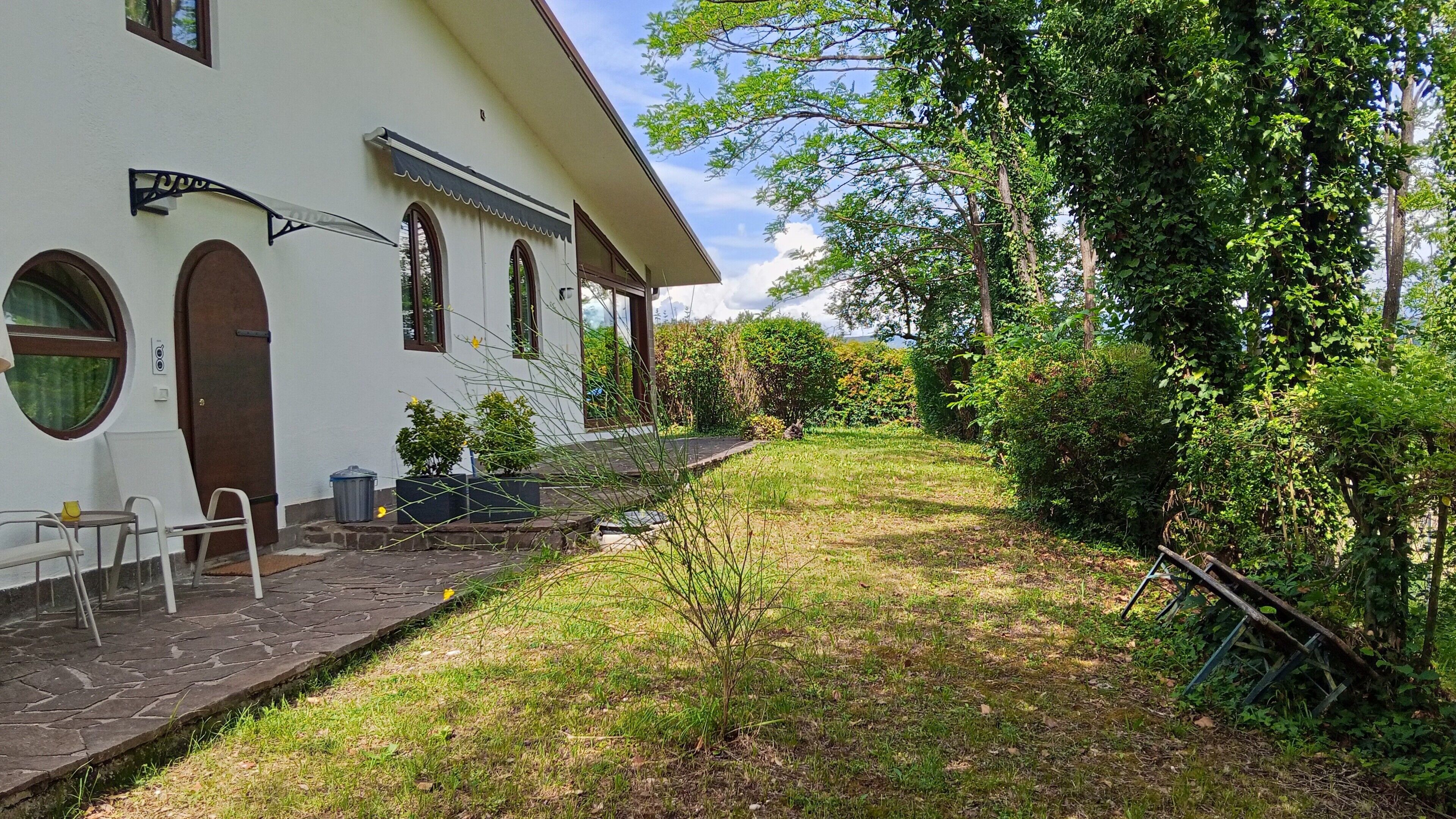 A white building with arched windows, a covered porch, and a stone pathway leading to outdoor seating.