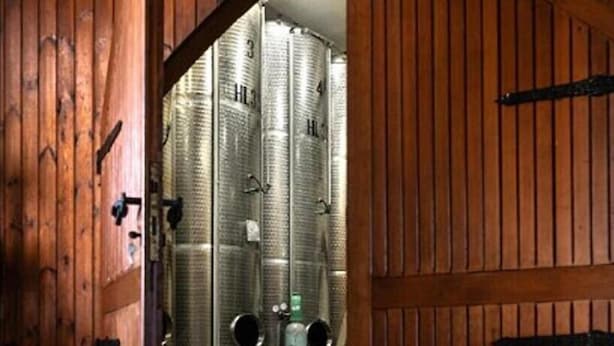 A wooden door leading to a room with industrial-style metal tanks and a metal barrel.