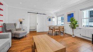 A spacious living room with a wooden floor, a grey sofa, a wooden coffee table, a dining area with a table and chairs, a large mirror, and a potted plant. - A Scholar s Gallery - Bloomsbury - by Frankie Says (London)