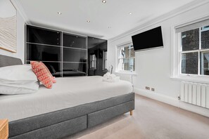 A modern bedroom with a large bed, a walk-in closet, a flat-screen TV, and a window with a view of a brick building. - A Scholar s Gallery - Bloomsbury - by Frankie Says (London)
