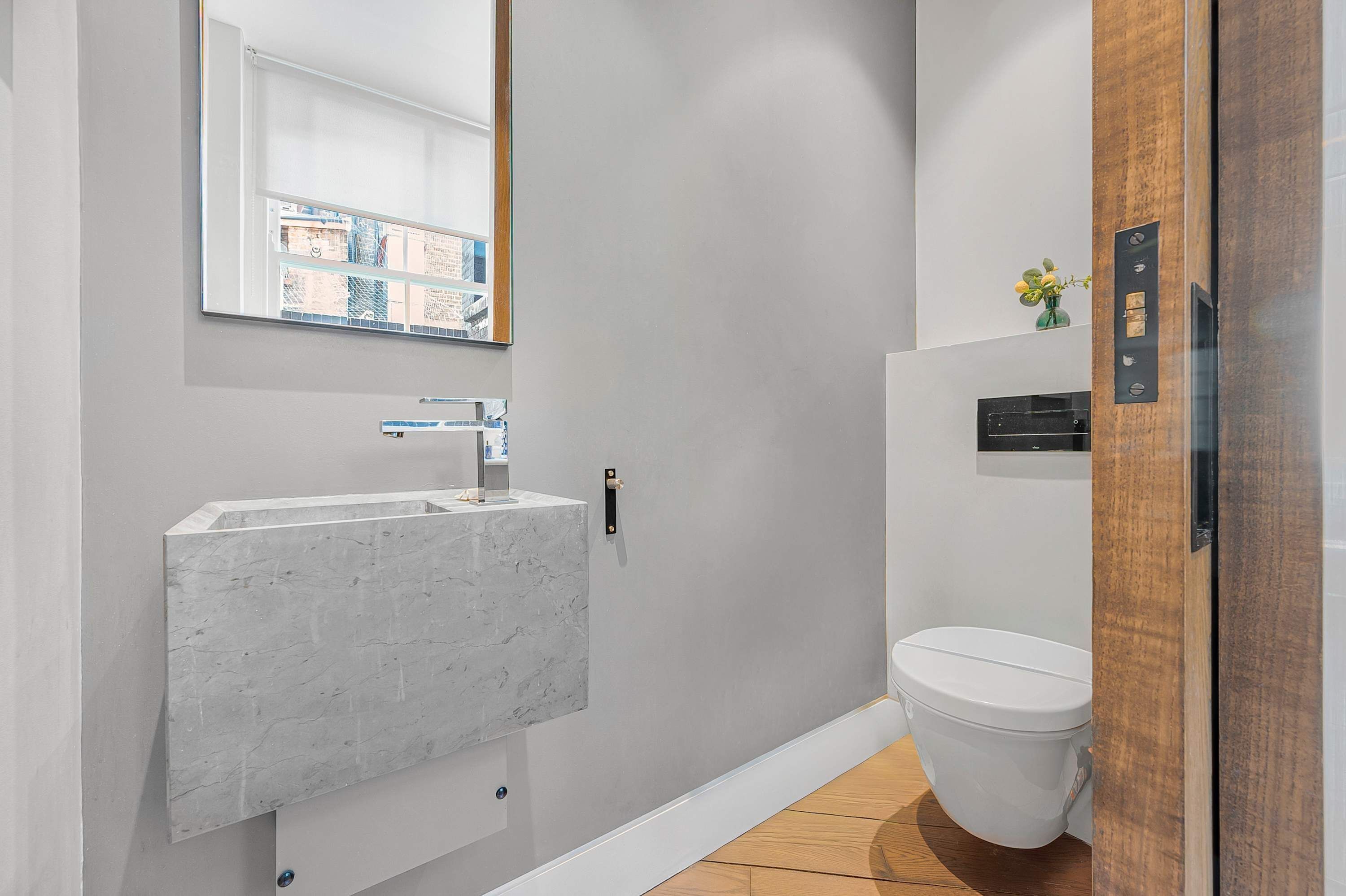 A modern bathroom with a marble sink, a toilet, and a wooden door.