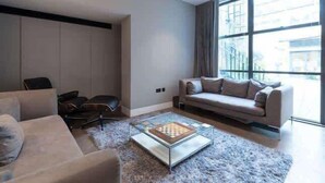 A modern living room with a sofa, armchairs, a glass coffee table, and a large window. - Monochrome Majesty - Soho - by Frankie Says (London)