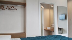 A bedroom with a bed, a wooden bench, a hanging clothes rack, a bathroom with a sink and mirror, and a television mounted on the wall. - Giardino del Tempo (Lizzanello)