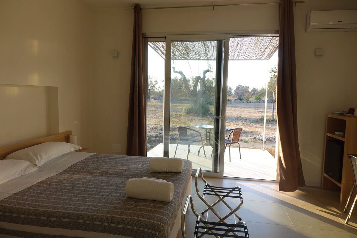A bedroom with a bed, a chair, and a view of the outdoors.