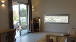 A modern living room with a sliding glass door leading to an outdoor area, a wooden desk, a comfortable sofa, and a small shelf with decorative items. - Giardino del Tempo (Lizzanello)