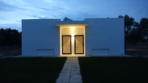 A modern building with a central entrance, a pathway leading to it, and a clear sky in the background. - Giardino del Tempo (Lizzanello)
