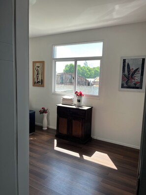 A room with a large window, a dark wooden cabinet, and two wall-mounted artworks.