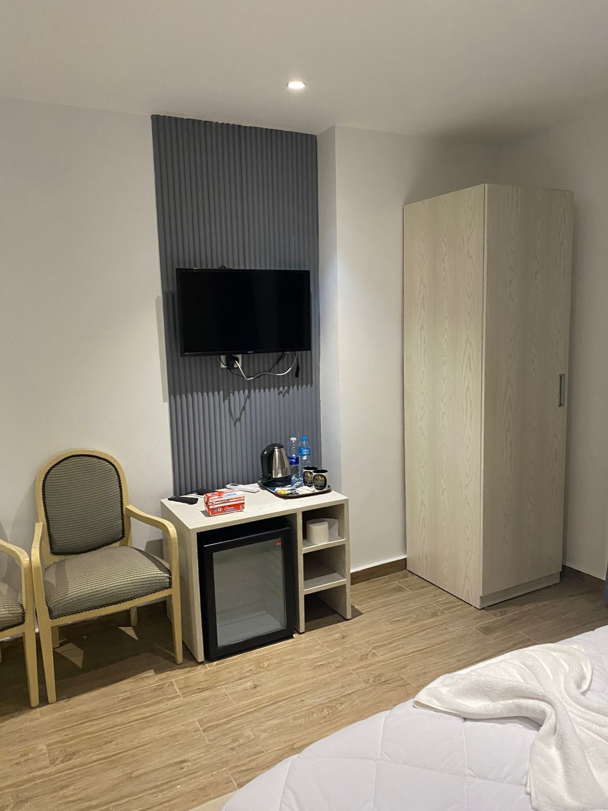 Habitación de hotel con cama, escritorio con televisor, silla, armario y refrigerador pequeño.