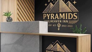 A reception desk with a wooden finish and a marble top. The wall behind features a black backdrop with the text "PYRAMIDS HEAVEN INN" and a logo of pyramids. - Pyramids heavin inn (Giza)