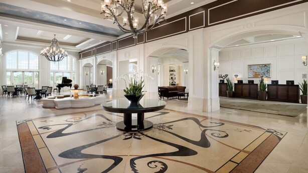 A spacious lobby with a grand chandelier, a piano, and a reception desk.