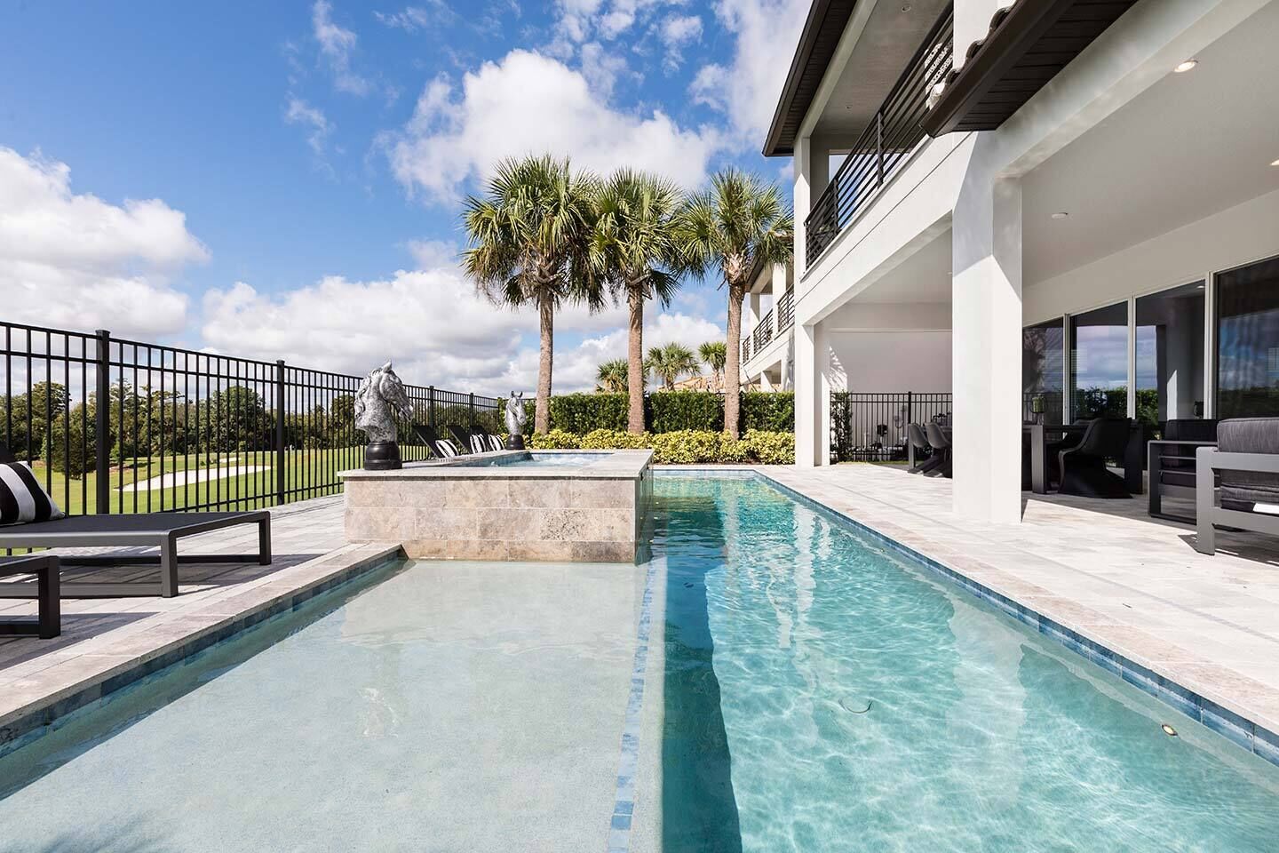 Une piscine bordée de pierres, des palmiers et un bâtiment moderne doté d’un balcon.