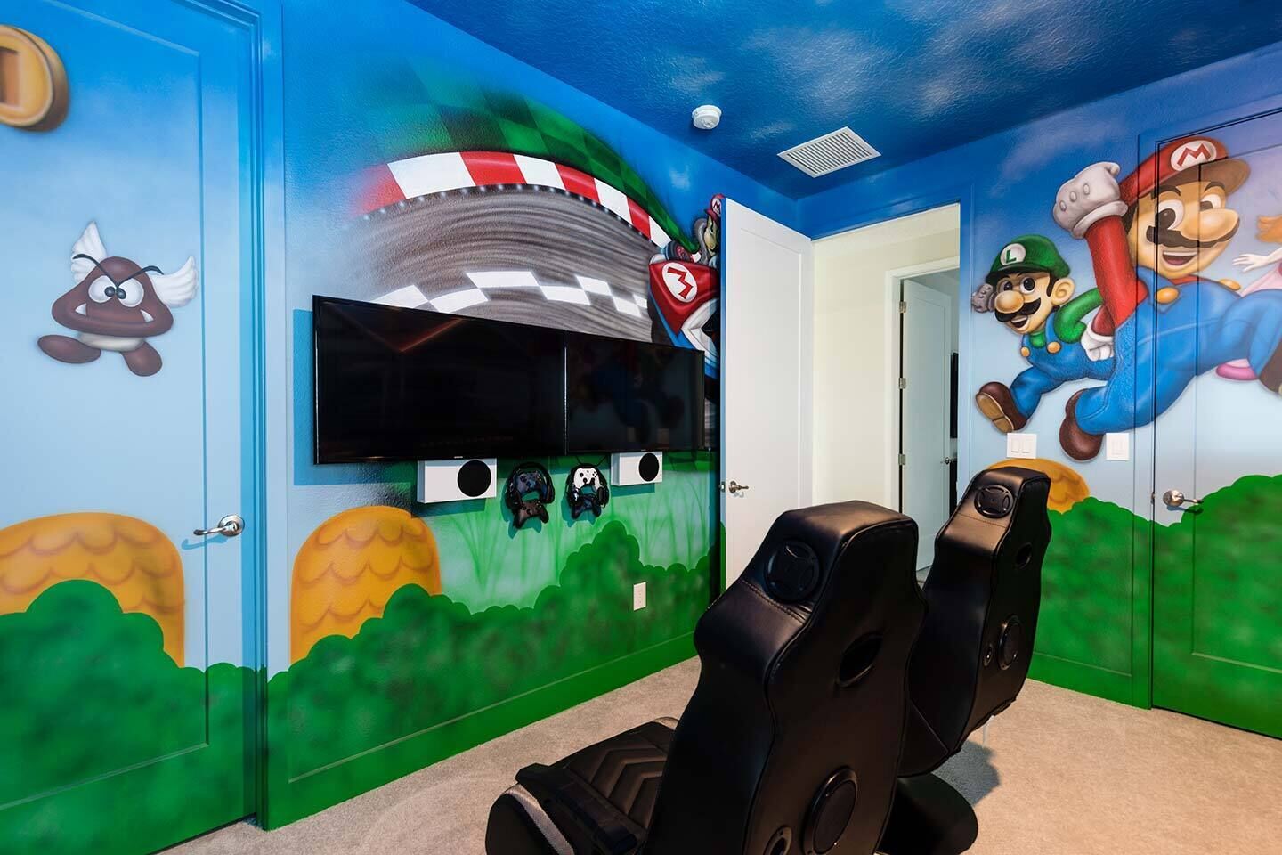 Une salle de jeux équipée d’un grand écran, de fauteuils de jeu et de décorations sur le thème de Mario.