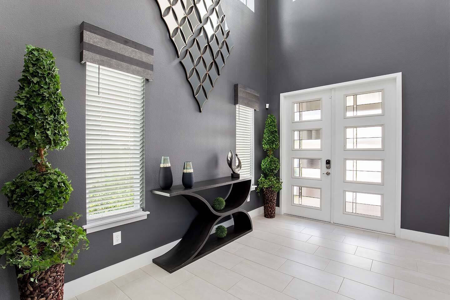 Un couloir moderne avec un mur gris foncé, une porte blanche dotée de panneaux de verre et une console noire agrémentée d’objets décoratifs.