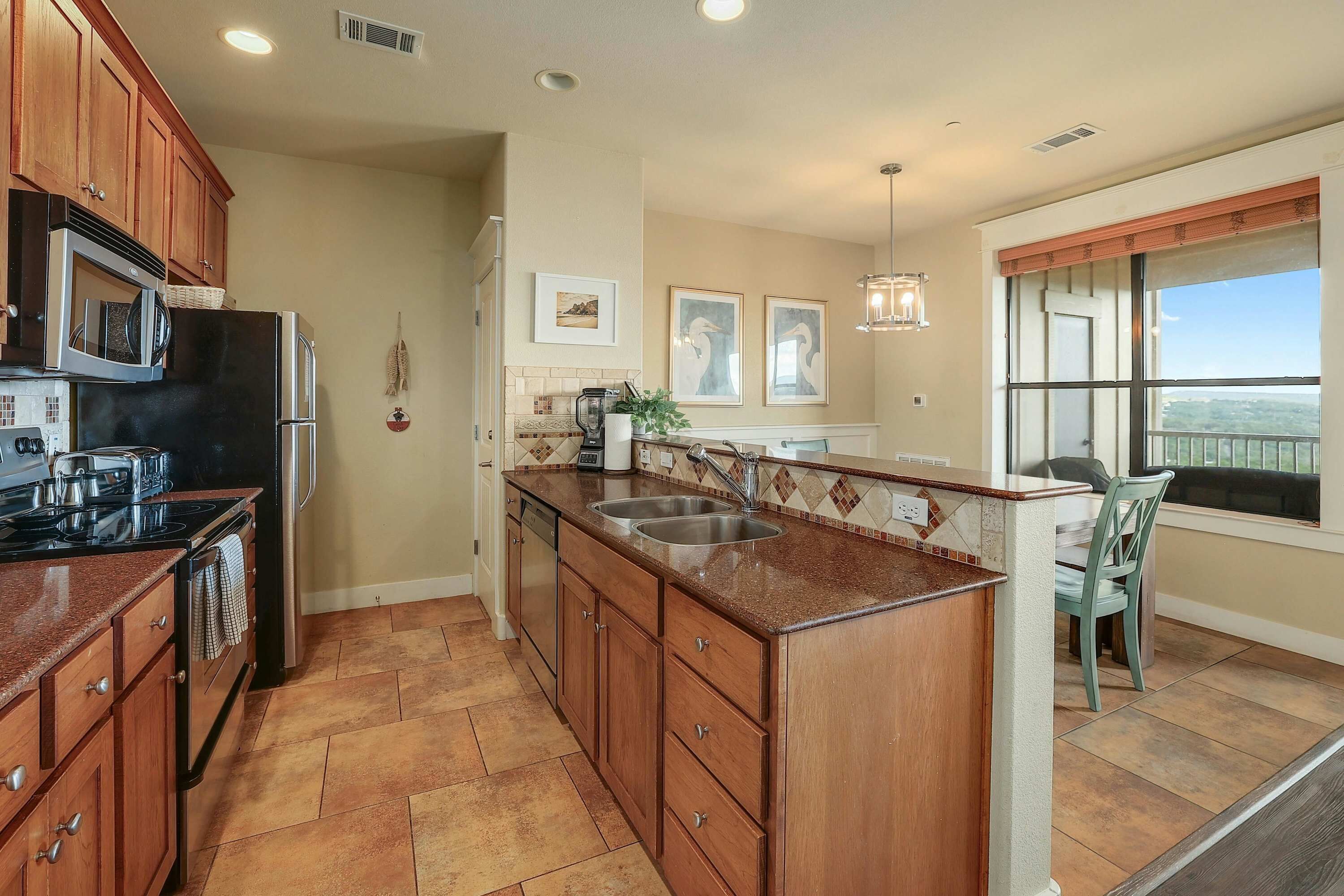 A kitchen with wooden cabinets, a black refrigerator, a stainless steel sink, and a window with a view.