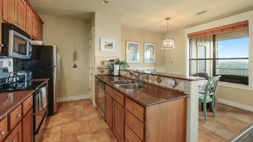 A kitchen with wooden cabinets, a black refrigerator, a stainless steel sink, and a window with a view.