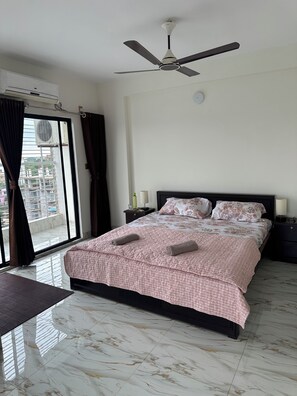 A bedroom with a bed, a ceiling fan, a window with curtains, and a view of buildings outside. - Specious Wonderful 2 AC & 2 NON AC bedroom apartment in West Khulshi,Chittagong (Chittagong)