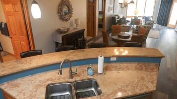 A kitchen with granite countertops, a double sink, and a dining area with a round table and chairs.