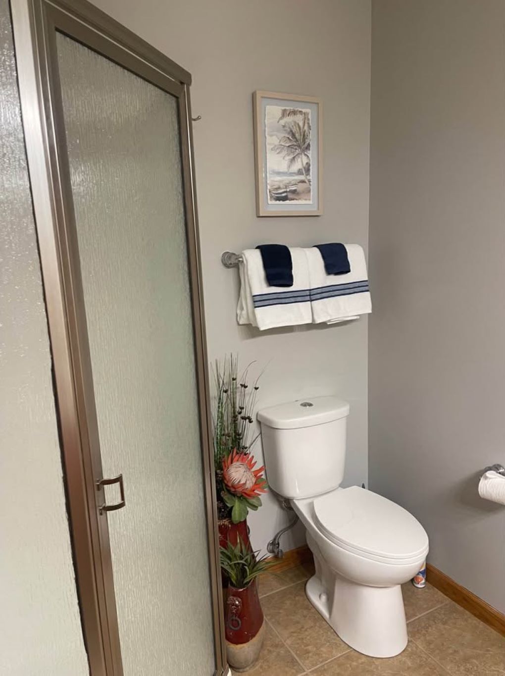 Une salle de bain avec des toilettes, un porte-serviettes avec une serviette, un tableau encadré au mur et une plante en pot.