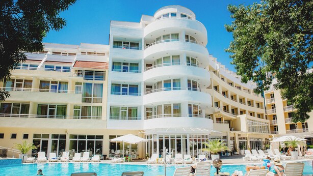 A hotel with a pool area, multiple balconies, and a clear blue sky.