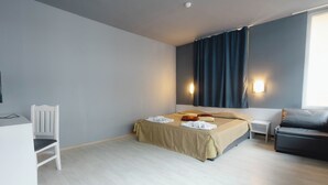 A hotel room with a bed, a desk, a chair, a sofa, and a window with curtains.