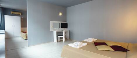 A modern hotel room with a large bed, a desk with a chair, a television, and a wardrobe.