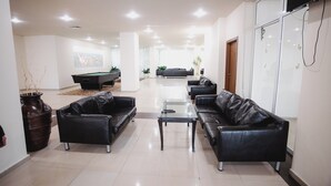 A spacious living area with black leather sofas, a glass coffee table, and a pool table.