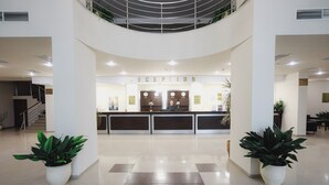A reception area with a modern design, featuring a reception desk, potted plants, and a staircase in the background.
