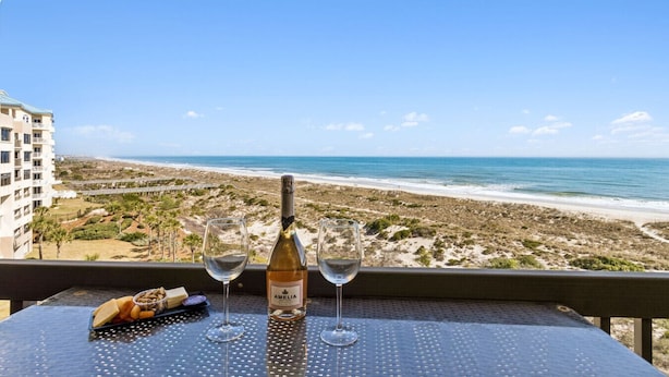 A table with a bottle of Amelia wine, two glasses, and a cheese platter overlooking a beach. - Amelia Surf & Racquet Club B164 | 6th Floor Oceanfront | Pools | Tennis Courts | Sleeps 8 (Fernandina Beach)