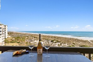 Une table avec une bouteille de vin Amelia, deux verres et une assiette de fromages, le tout placé face à une plage.