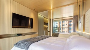 A modern hotel room with a large bed, a flat-screen TV mounted on the wall, and a view of the city through large windows. - Luxo em rua icônica no Itaim Bibi (Sao Paulo)