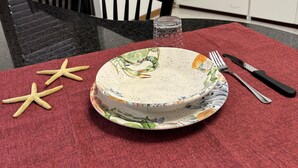 Uma mesa de jantar com um prato, talheres e uma estrela-do-mar sobre um jogo americano vermelho.