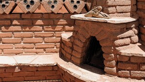 A brick oven structure with a chimney, surrounded by a brick wall with decorative patterns.