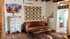 A cozy living room with a brown sofa, wooden coffee table, patterned rugs, a decorative cabinet, and a wall-mounted air conditioner.