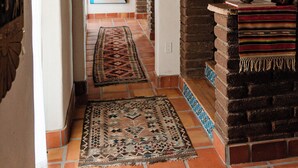 A hallway with a rustic brick fireplace, a patterned rug, and a framed picture on the wall.