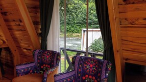 A wooden cabin with two patterned chairs by a window overlooking a river. - Yeşil Düş Bungalov (Findikli)