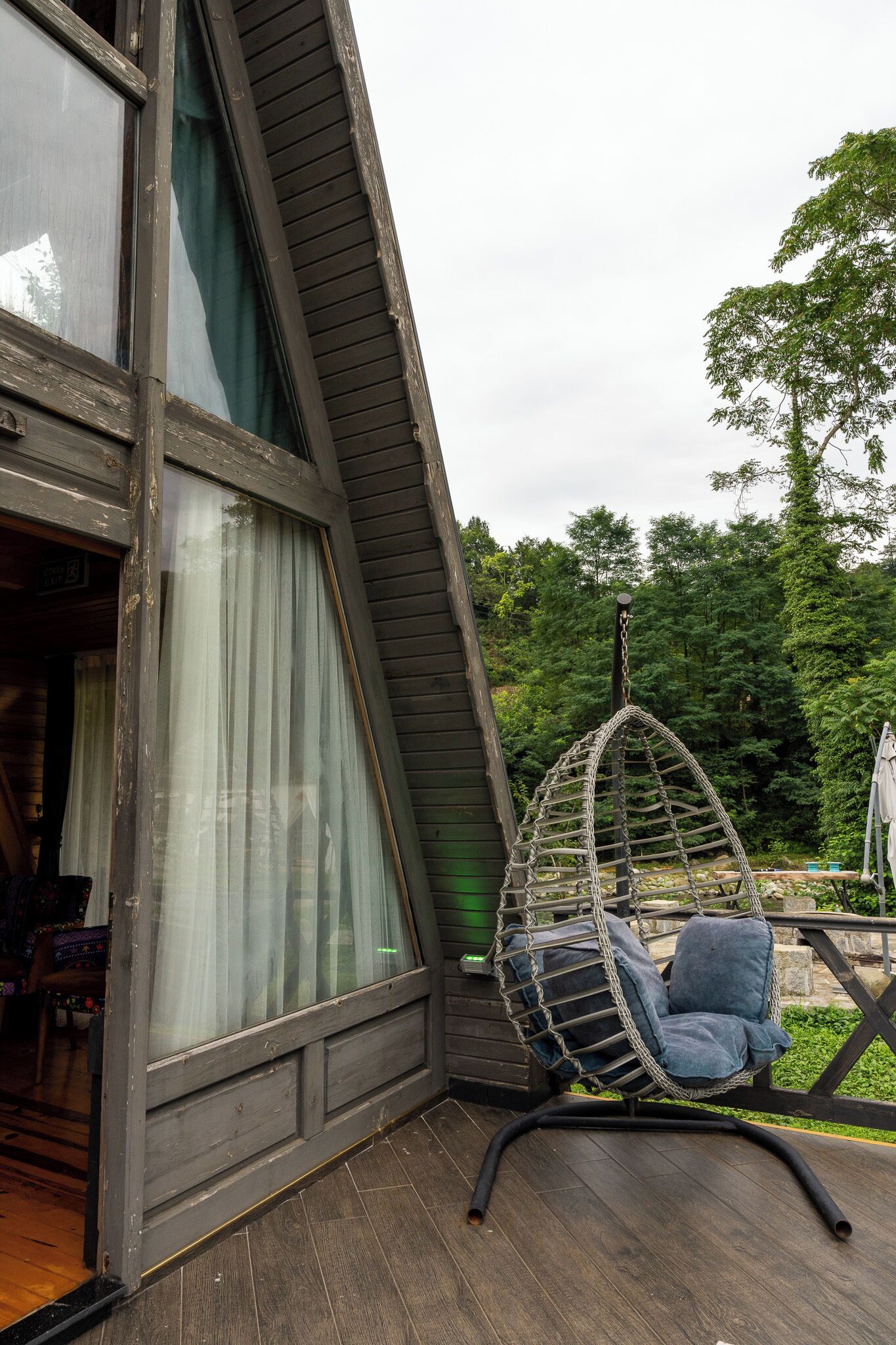A wooden deck with a hanging chair and a large window with curtains.
