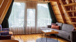 A cozy living room with a wooden floor, a gray sofa, a wooden coffee table, and a large window with sheer curtains. - Yeşil Düş Bungalov (Findikli)